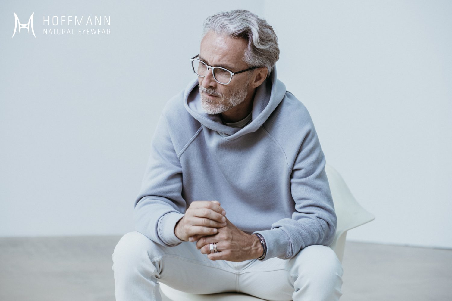 Ein älterer Mann mit blauem Kapuzenpullover trägt eine Hornbrille von Hoffmann Natural Eyewear.